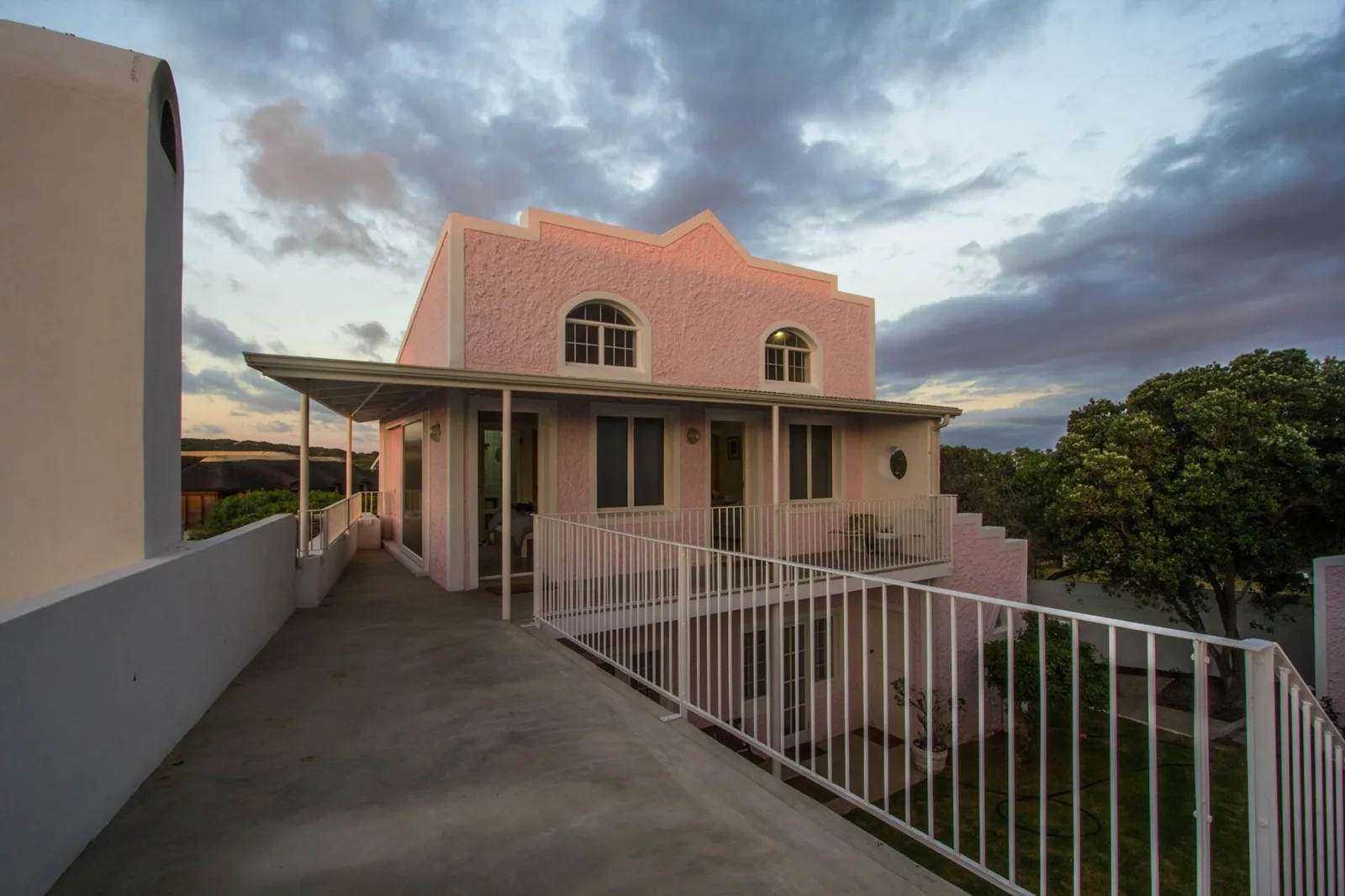 Pink house with arched windows seen from the driveway beside a white railing