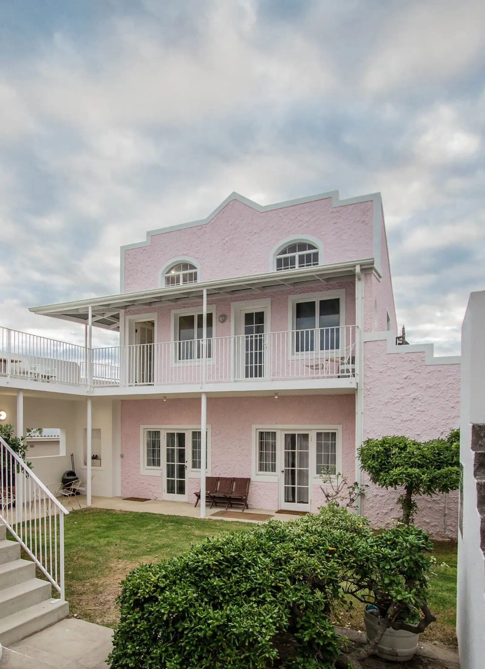 Pink house with white balconies above a garden and stairs