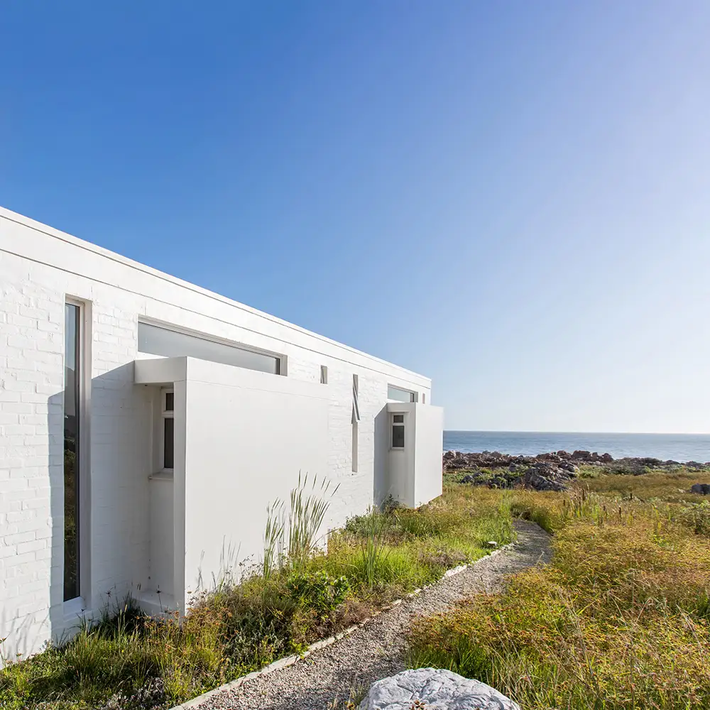 Long white wall of the addition with a narrow window, ocean in the distance