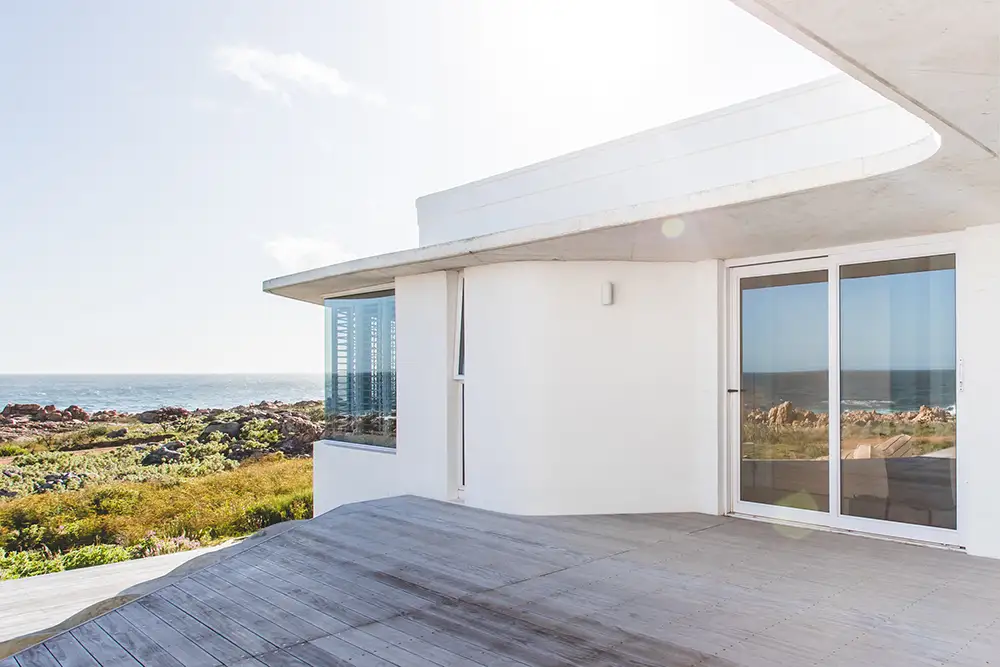 Timber deck beside the white addition with sliding doors and an ocean view