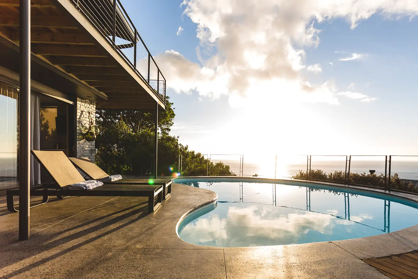 Swimming pool and deck below an overhanging balcony at sunset