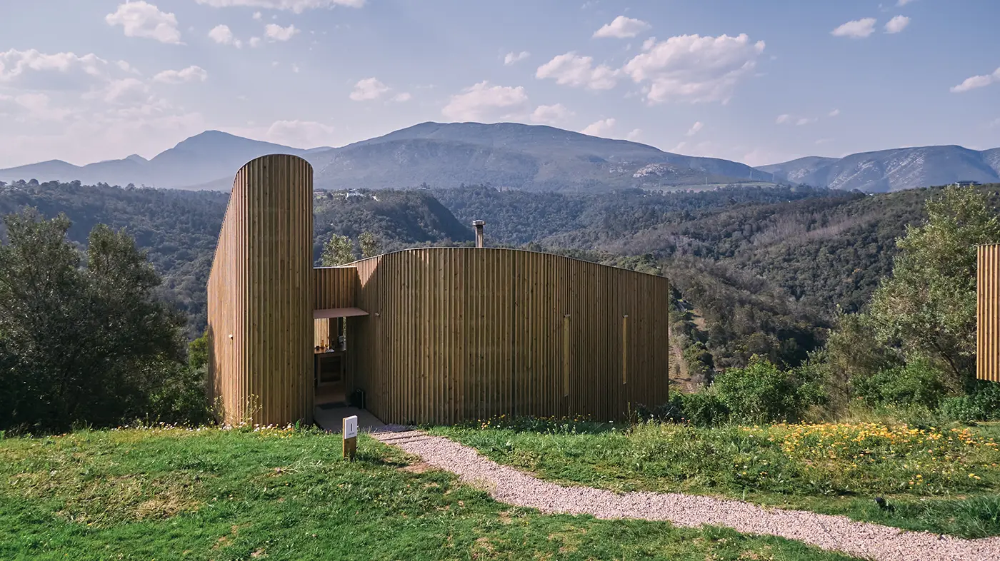 Cabin in a meadow with a path and mountains behind