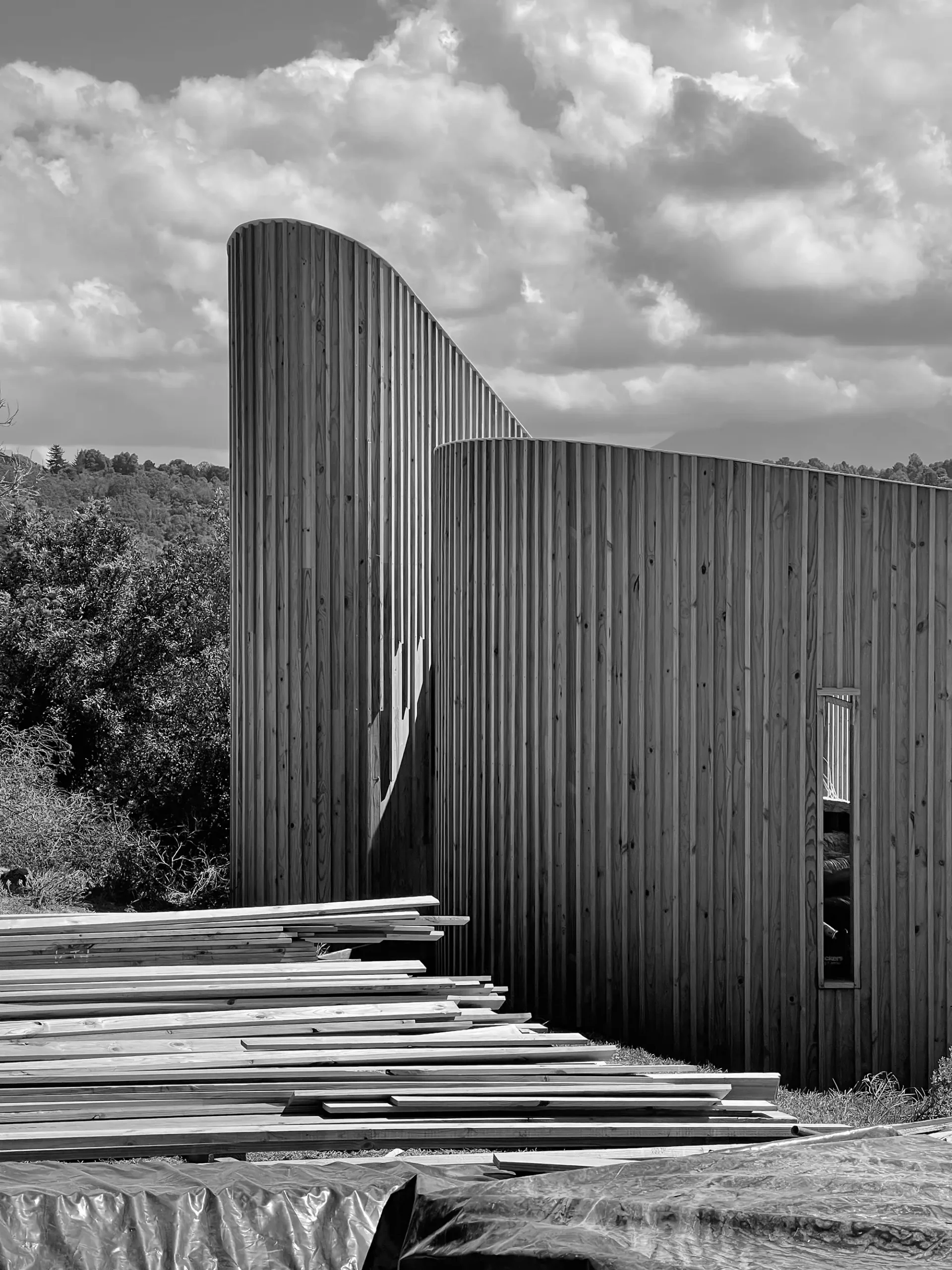 Curved timber-clad walls under construction with timber stacked in front
