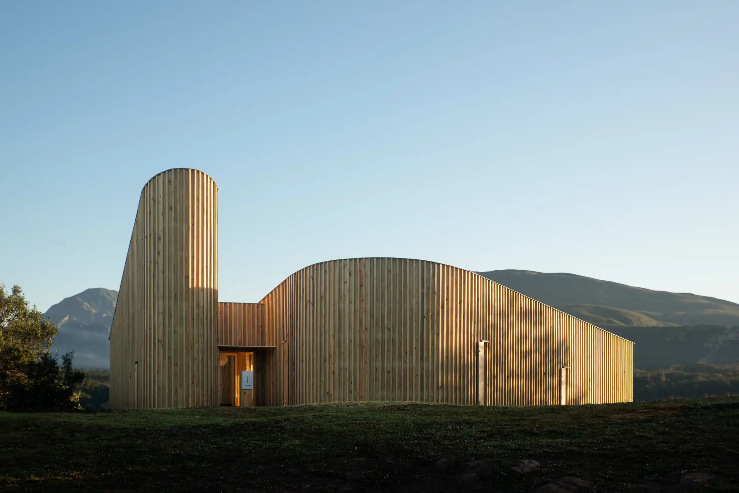 Finished cabin at dusk: a tall curved timber tower and a rounded volume
